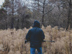 man in black jacket and blue denim jeans standing on brown grass field during daytime