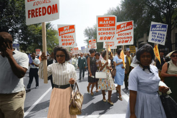 Demonstrators walk along a street holding signs demanding the right to vote and equal civil rights at the March on Washington