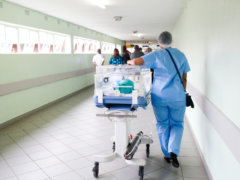 person walking on hallway in blue scrub suit near incubator