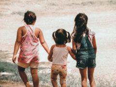 three girls holding each other hand walking towards brown soil