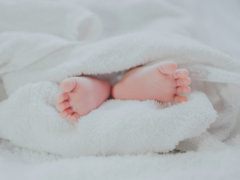 barefooted baby covering white blanket