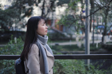 woman in gray scarf and coat standing near bridge