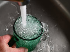 a person's hand is holding a green cup with water coming out of it