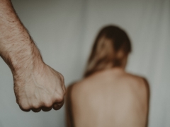 Aggressive abusive anonymous man clenching fist while insulting unrecognizable vulnerable female sitting on blurred background in light room during violence