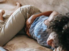 From above of crop anonymous African American female lying on couch and touching belly while having stomach ache