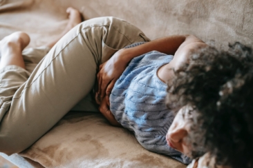 From above of crop anonymous African American female lying on couch and touching belly while having stomach ache