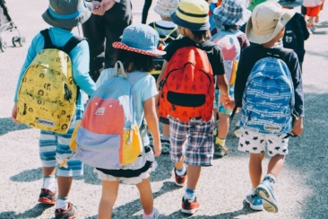 group of people wearing white and orange backpacks walking on gray concrete pavement during daytime